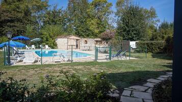 A backyard with a swimming pool, lounge chairs, and a stone building.