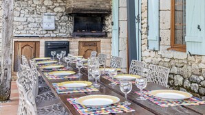 Un espace de restauration en plein air agrémenté d’un mur en pierre, d’un four en briques et d’une table en bois dressée pour un repas.