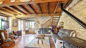 Un salon rustique avec un mur en pierre, des poutres en bois, une cheminée et un escalier.