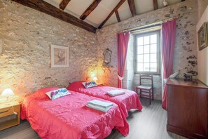 A room with two beds, a wooden nightstand, a chair, a wooden cabinet, and a window with curtains. - Homerez - House in Thenac (Thenac)