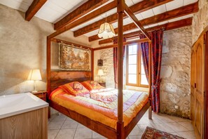 A four-poster bed with a colorful quilt, a stone wall, a wooden ceiling, and a painting above the bed. - Homerez - House in Thenac (Thenac)