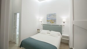 A modern bedroom with a bed, bedside tables, and a painting on the wall. - GR Suites Boutique Catedral AP-B (Málaga)