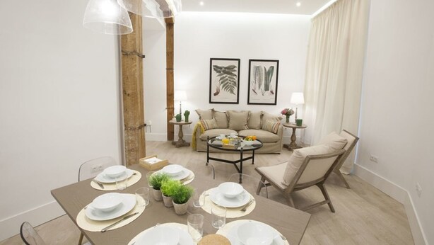 A modern living room with a sofa, a coffee table, and a dining area set for four. - GR Suites Boutique Catedral AP-B (Málaga)