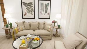 A living room with a sofa, a coffee table with breakfast items, and two framed botanical prints on the wall. - GR Suites Boutique Catedral AP-B (Málaga)