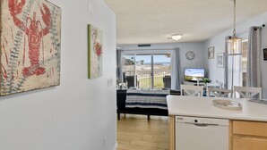 Una cocina moderna con lavavajillas, un comedor con televisor y un balcón con vistas al mar.