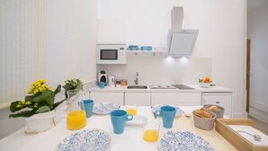 Una cocina moderna con armarios blancos, un microondas y un lavabo. Hay platos y tazas azules y blancos, y un bol de fruta en la encimera.
