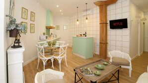 Uma sala de estar com área de jantar, cozinha e televisão fixada na parede.