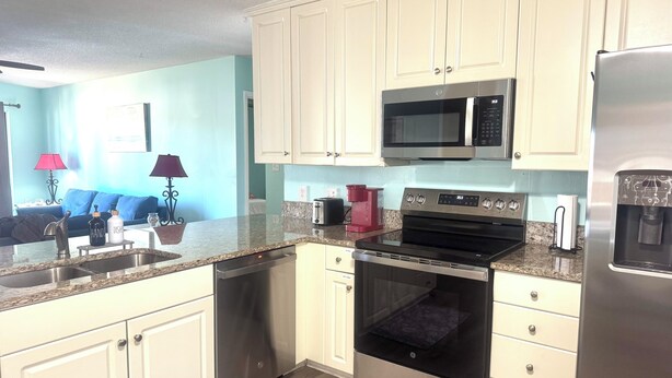 A modern kitchen with white cabinets, stainless steel appliances, a microwave, oven, and dishwasher. - Cozy Condo Short Walk to the Beach (Miramar Beach)