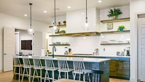 A modern kitchen with white cabinetry, a central island with bar stools, pendant lighting, and decorative plants.