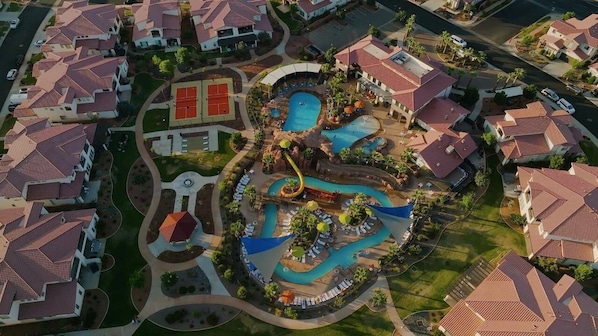 Ein Luftbild eines Resorts mit mehreren Schwimmbecken, einer Wasserrutsche und einem Tennisplatz.