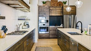 A modern kitchen with a central island, built-in ovens, a stainless steel refrigerator, and wooden cabinetry.