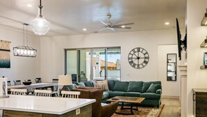 A modern living room with a green sofa, a coffee table, and a dining area with a chandelier.