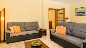 Two grey sofas with orange cushions, a wooden side table, and a green tray table in a living room with cream walls and a wooden door. - Jadlyn Yellow Villa, Falésia Beach, Albufeira, AC, WiFi, Swimming Pool !New! (Albufeira)