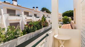 A residential building with multiple balconies, white walls, and a small garden area with various plants and flowers. - Jadlyn Yellow Villa, Falésia Beach, Albufeira, AC, WiFi, Swimming Pool !New! (Albufeira)
