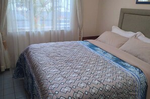A neatly made bed with a patterned bedspread, a headboard, and a window with curtains. - Cottage Sleeps 4 with Pool (Harare)