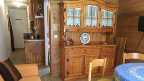 Un interior acogedor de madera con un sofá, una mesa de comedor con mantel azul y un aparador de madera con puertas de vidrio.