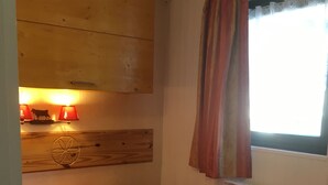 Una habitación pequeña con dos camas, cabeceros de madera, un radiador y una ventana con cortinas.