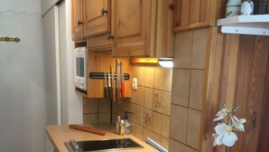 Una cocina con armarios de madera, un lavamanos de acero inoxidable, un microondas y una orquídea en maceta.