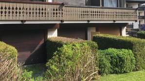 Un edificio de varios pisos con balcones, techo plano y vista a una montaña boscosa.