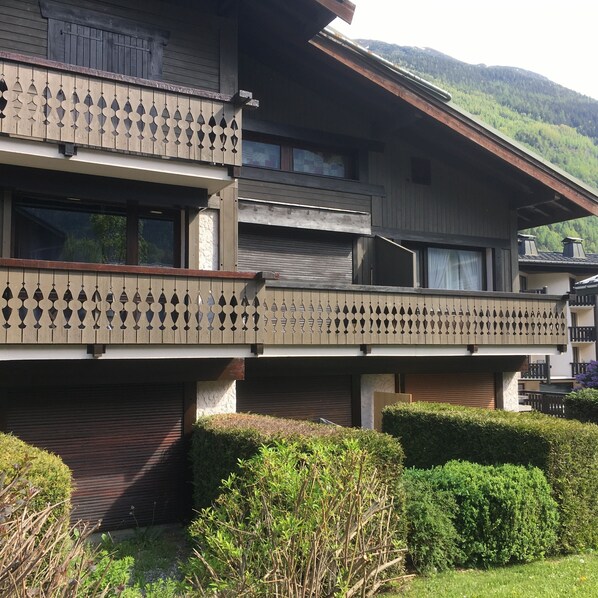 A multi-story building with balconies, a flat roof, and a view of a forested mountain.