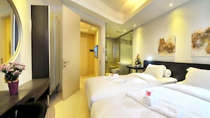A hotel room with two beds, a large mirror, a wooden desk, and a bathroom visible through an open door.