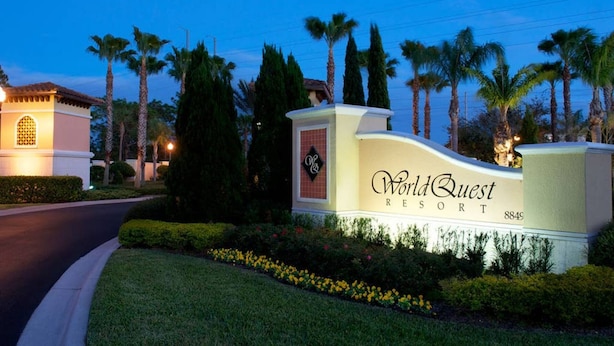 Skilt for WorldQuest Resort med en velholdt have og palmer i baggrunden.