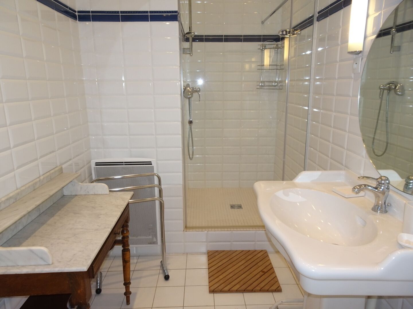 Un baño con encimera de mármol, mueble de tocador de madera, ducha con mampara de vidrio y lavabo blanco.