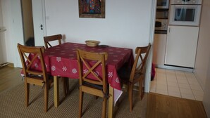 Un coin repas avec une table dressée pour quatre personnes, des chaises en bois, une nappe rouge et un tableau accroché au mur.