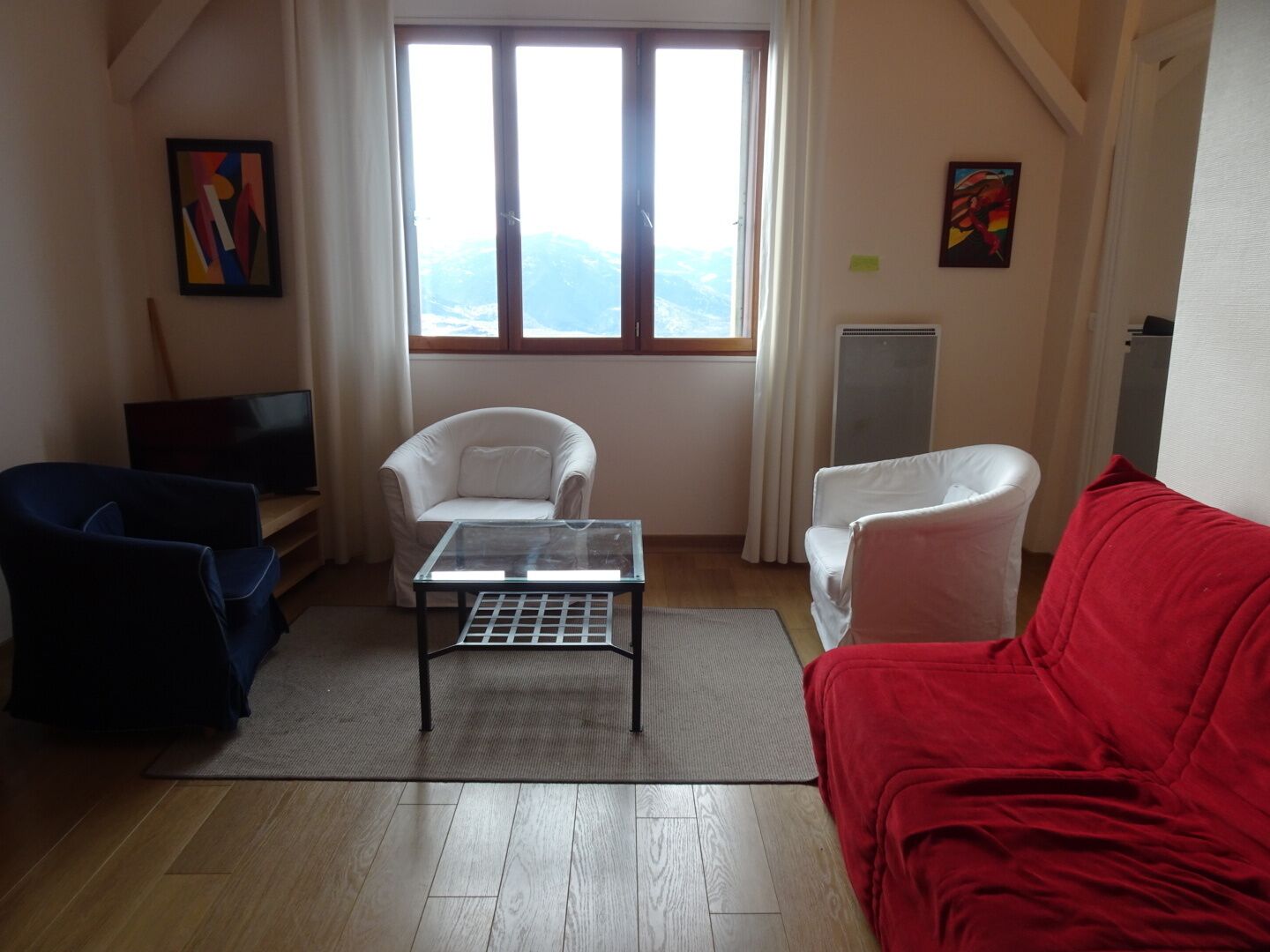 A living room with a TV, two white armchairs, a red sofa, and a glass coffee table.