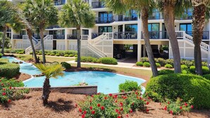 A multi-story hotel with a pool, palm trees, and red flowers. - Crescent C1D - Beach - Pool - Tennis - Very Nice! (Pawleys Island)
