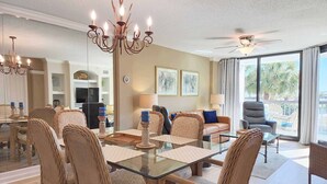 A spacious living area with a glass dining table surrounded by wicker chairs, a chandelier, and a ceiling fan. - Crescent C1D - Beach - Pool - Tennis - Very Nice! (Pawleys Island)