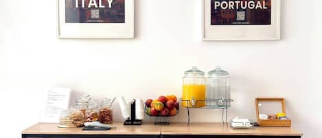 A breakfast table with food, a drink dispenser, and two framed posters of Italy and Portugal.