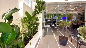 Un pasillo interior con plantas en macetas, un escaparate de vidrio y suelo de baldosas.