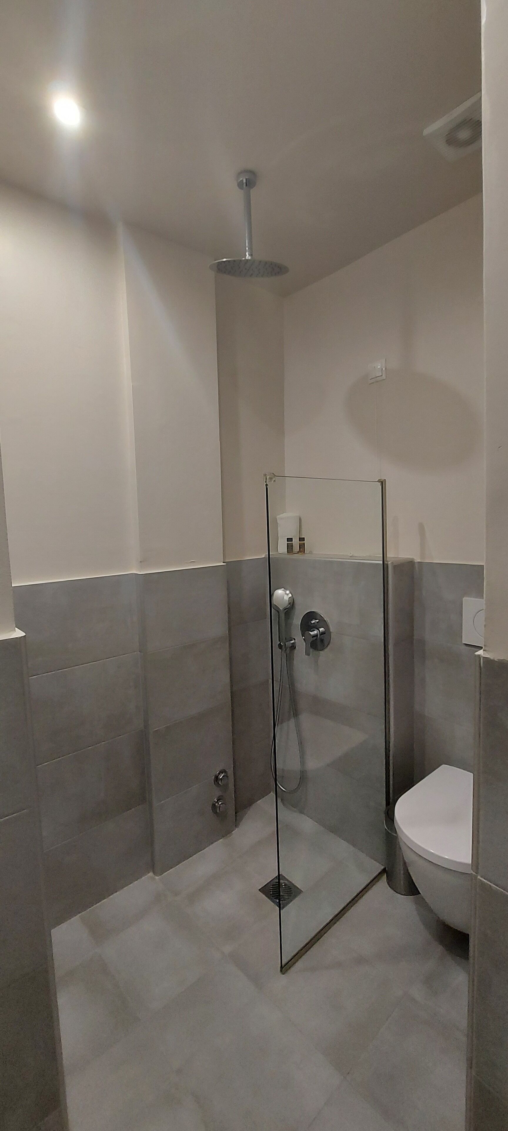 A modern bathroom with a glass-enclosed shower, a white toilet, and grey tiled walls.