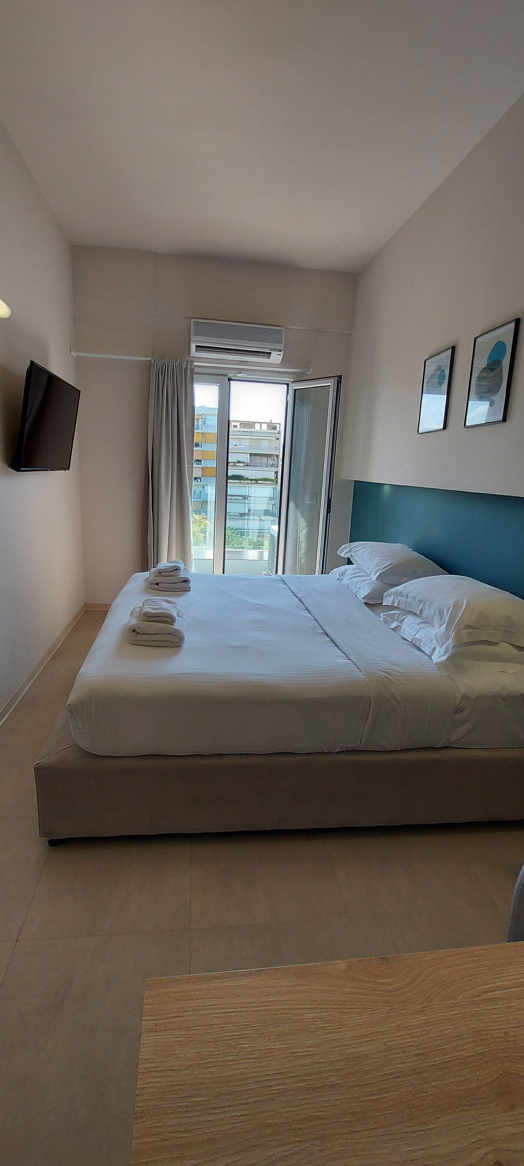 A hotel room with a large bed, a flat-screen TV mounted on the wall, and a window with curtains.