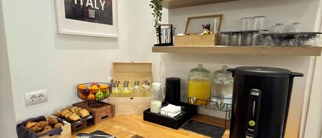 A corner kitchenette with a coffee maker, a fruit basket, and a framed picture of Italy.