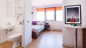 Une chambre à coucher avec un lit, une table de chevet, une fenêtre avec des stores orange et un tableau encadré au mur.
