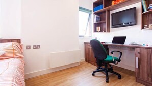 Une chambre à coucher avec un lit, un bureau avec un ordinateur, une chaise et un téléviseur fixé au mur.