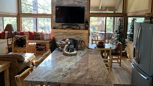 A cozy cabin interior with a stone fireplace, a large flat-screen TV, wooden furniture, and a view of the surrounding forest. - Northstar Mountain charm & luxury, near shuttle, 10 minutes to slopes, sleeps 6, (Truckee)
