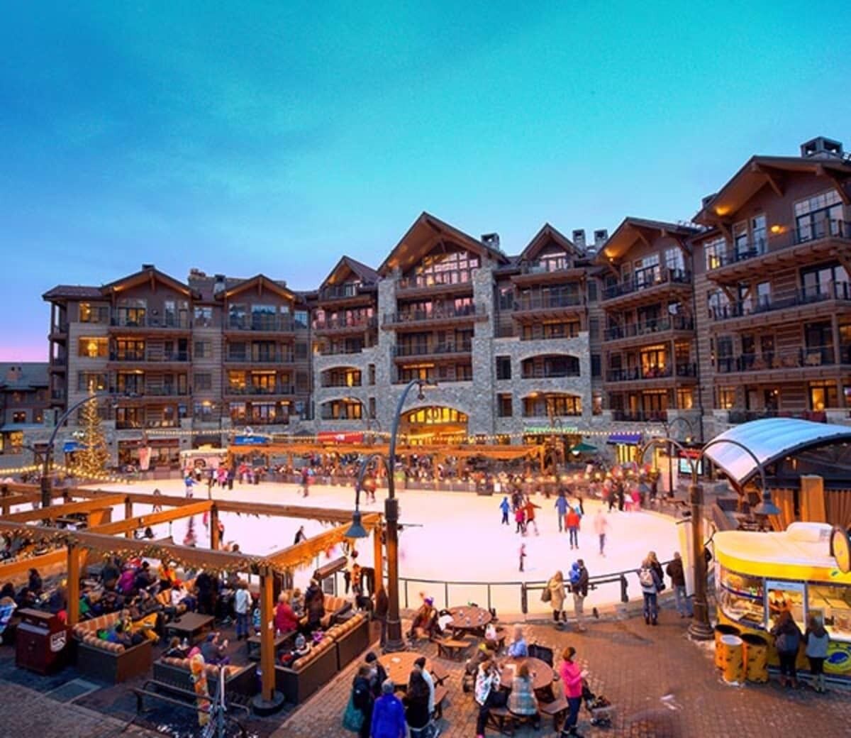 Ein mehrstöckiges Hotel mit Balkonen, einem zentralen Innenhof mit einer Eislaufbahn und Außenbereichen mit Sitzgelegenheiten.