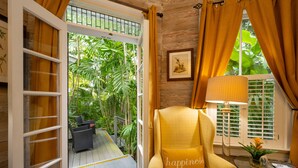 A room with a yellow armchair, a glass coffee table, and a view of a wooden deck and tropical plants. - The Mermaid & Alligator (Key West)