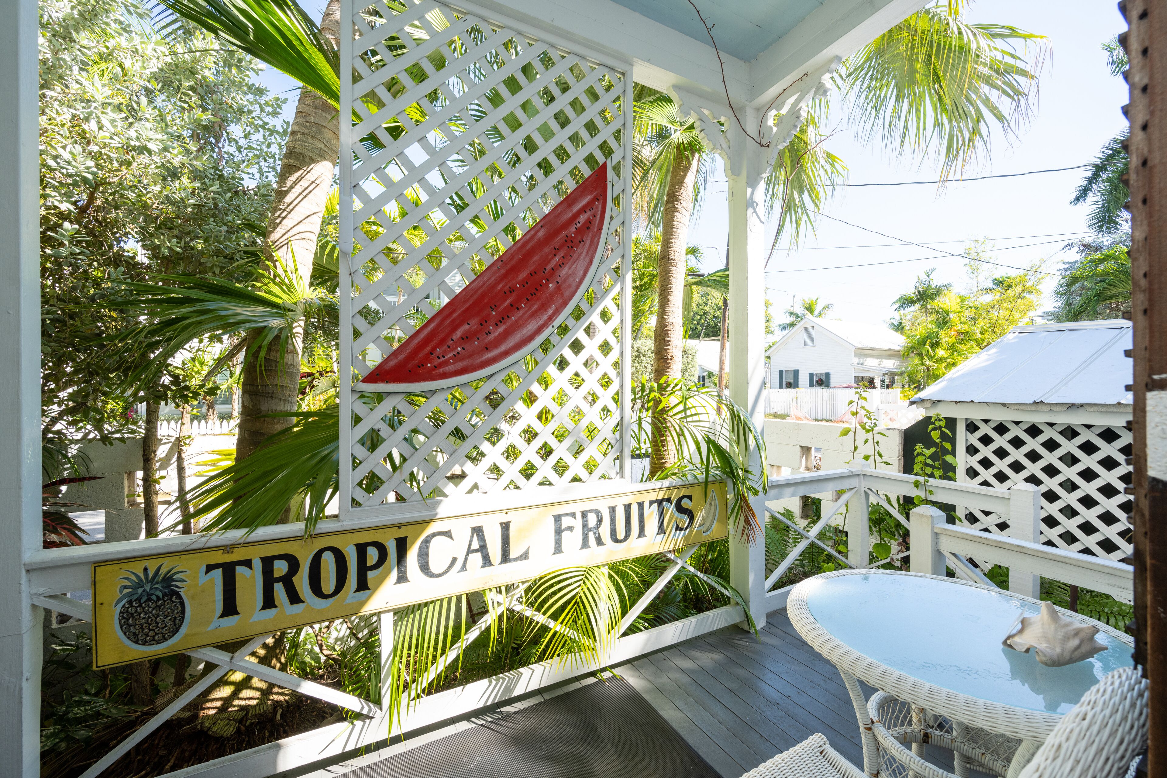 Un espace extérieur abrité, agrémenté d’une enseigne indiquant « Fruits tropicaux » et d’une table avec des chaises.
