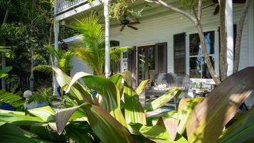 A two-story house with a balcony, surrounded by lush tropical plants.