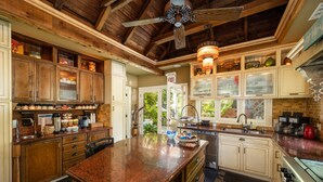 A spacious kitchen with wooden cabinets, a granite countertop, and a ceiling fan. - The Mermaid & Alligator (Key West)