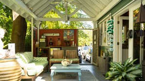 A cozy outdoor seating area with a wooden bench and a table, surrounded by potted plants and a coffee and tea sign. - The Mermaid & Alligator (Key West)