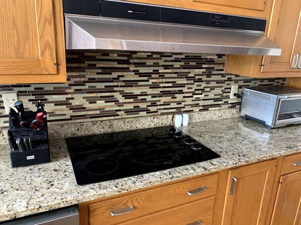 Kitchen features a black induction cooktop, stainless steel range hood, and wooden cabinets.