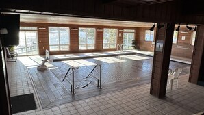 A wooden interior with large windows, a tiled floor, and a pool area with a sign.