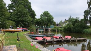 Een kade aan de rivier met boten, een gazon en een met stenen bestraat pad.