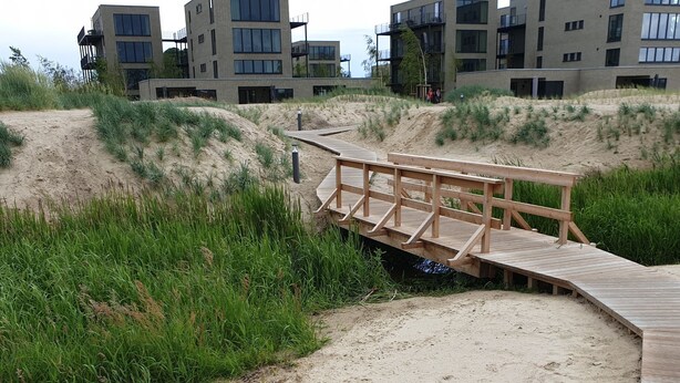 Een houten looppad dat leidt naar een modern gebouw met meerdere balkons en grote ramen.