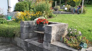 A stone bench with a planter in the center, surrounded by a garden with various plants and flowers. - Apartment mit Burgblick im Grünen, Familie Held (Burgthann)